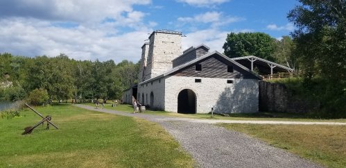 A historic stone building surrounded by greenery and a gravel path under a partly cloudy sky.