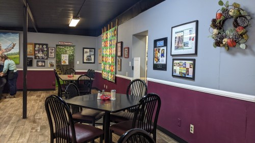 Cozy dining area with tables, colorful wall decor, and framed photos in a warm, inviting atmosphere.