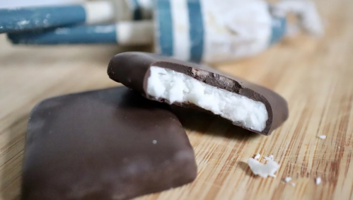 Two chocolate-covered bars with a creamy filling, placed on a wooden surface with a blue and white object in the background.