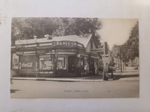 Black and white photo of Seavey's ice cream shop in Auburn, Maine, with vintage signage and nearby street view.