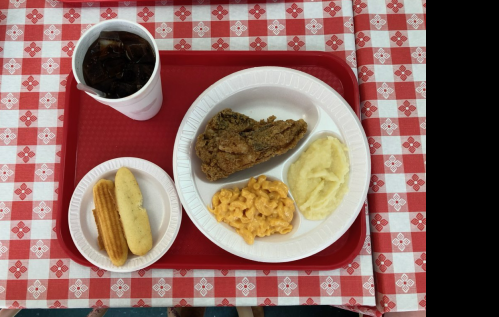 A cafeteria tray with fried chicken, mashed potatoes, macaroni and cheese, cornbread, and a drink.