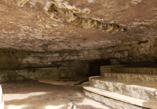 A spacious cave interior with stone steps and textured rock walls, illuminated by natural light.