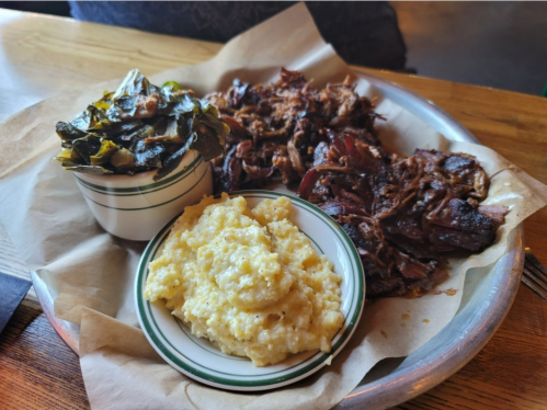A plate featuring pulled pork, collard greens, and creamy grits served in a rustic setting.