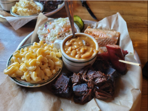 A plate of barbecue featuring brisket, sausage, baked beans, macaroni, coleslaw, and a slice of salmon.