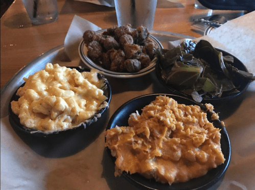 A plate with four bowls of Southern sides: macaroni and cheese, collard greens, sweet potato mash, and fried okra.
