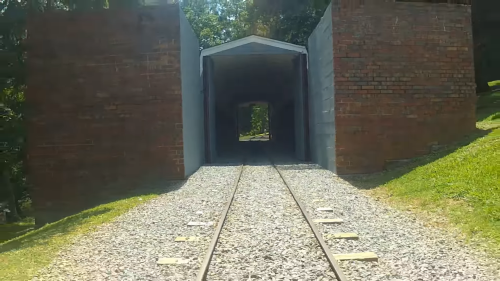 A view of a railway tunnel framed by brick walls, with tracks leading into the dark opening. Green grass surrounds the area.