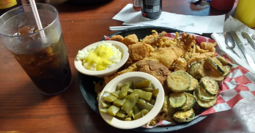 A plate of fried chicken, green beans, mashed potatoes with gravy, fried zucchini, and a glass of iced tea.