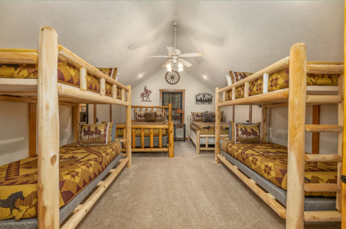 Cozy attic bedroom with wooden bunk beds, rustic decor, and a ceiling fan, creating a warm, inviting atmosphere.
