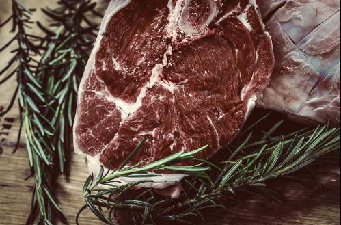 Close-up of a raw steak surrounded by fresh rosemary on a wooden surface.