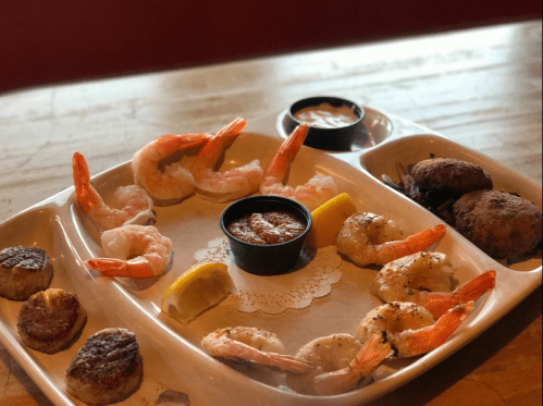 A seafood platter featuring shrimp, scallops, and dipping sauces, garnished with lemon on a white plate.