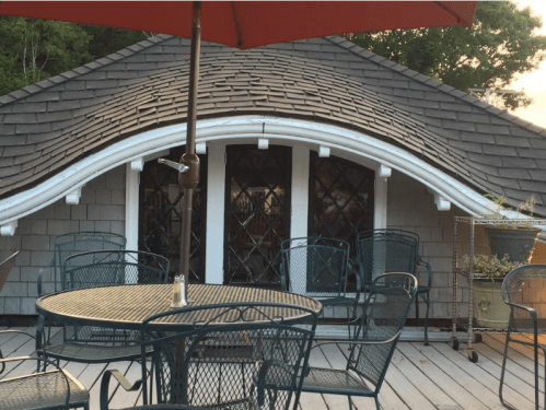 A cozy outdoor seating area with metal chairs and a table, featuring a unique curved roof and decorative windows.
