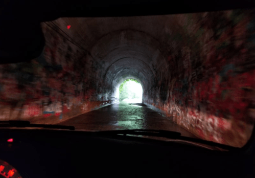 View from inside a vehicle approaching a colorful, graffiti-covered tunnel with light at the end.