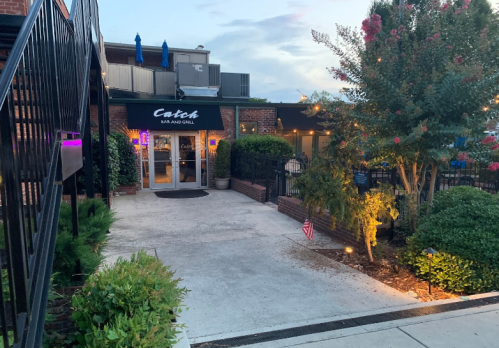 Exterior view of Catch Bar and Grill, featuring a welcoming entrance, greenery, and evening lighting.