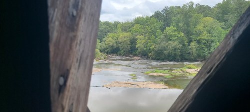 View of a serene river and lush greenery through a wooden frame, with cloudy skies above.