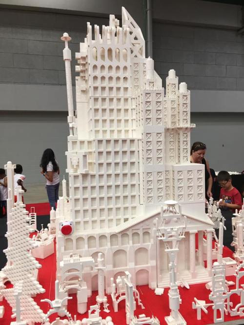 A large, intricate white building made of blocks, surrounded by smaller structures and people admiring the display.