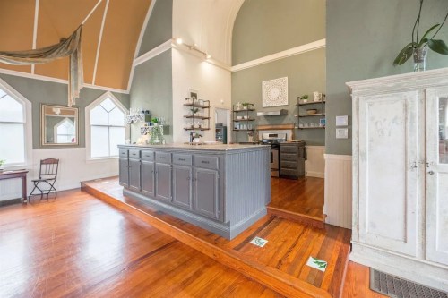 A spacious kitchen with a gray island, wooden floors, and large windows in a bright, airy room.