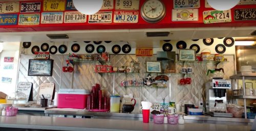 A retro diner counter with vintage decor, including records, license plates, and colorful drink dispensers.