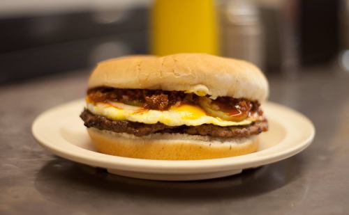 A hearty sandwich with a beef patty, fried egg, and sauce, served on a soft bun on a plate.