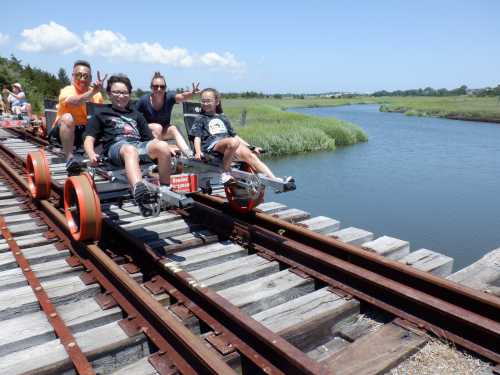 A group of four people poses on a rail bike beside a river, surrounded by greenery and blue skies.