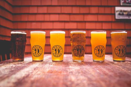 A row of six glasses of beer in various colors on a wooden table, with a rustic background.