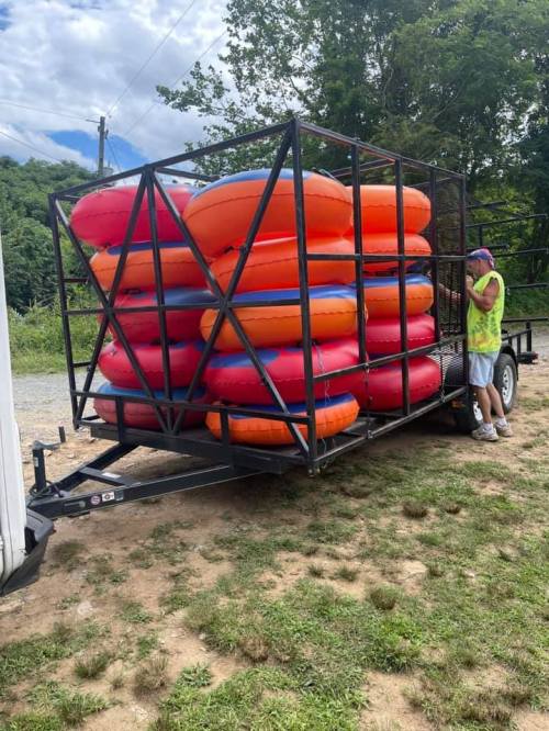 A trailer loaded with colorful inflatable tubes, with a person in a yellow vest standing nearby.