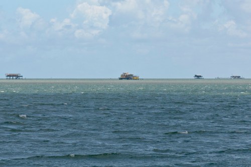 A view of the ocean with several fishing piers visible on the horizon under a partly cloudy sky.