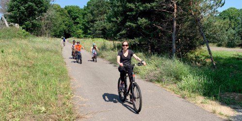 A group of people riding bicycles on a path surrounded by greenery and trees on a sunny day.