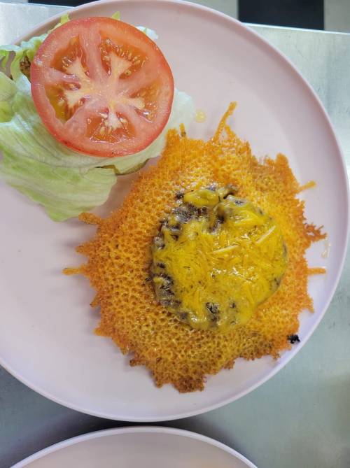 A plate featuring a crispy cheese dish with melted cheese, served with lettuce and a slice of tomato.
