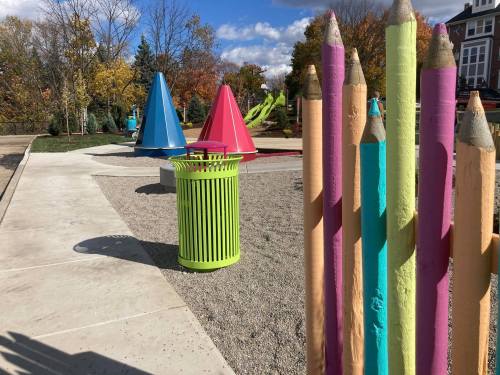 Colorful playground with large pencil sculptures, a green trash can, and vibrant triangular structures under a blue sky.