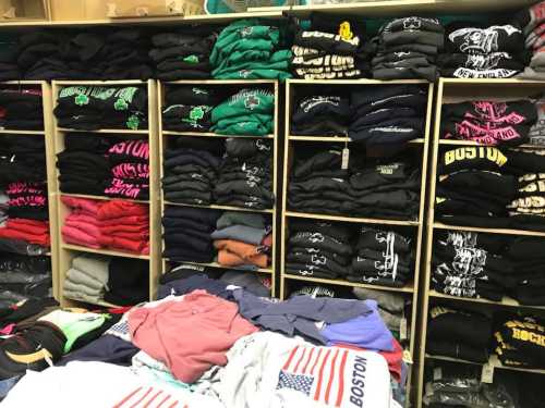 A display of neatly stacked t-shirts in various colors and designs on shelves and tables.