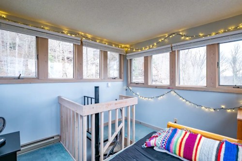 Cozy room with large windows, a wooden railing, and colorful string lights, featuring a bed with a vibrant blanket.