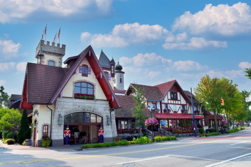Charming European-style building with flower boxes, flags, and guards in front, set against a blue sky with clouds.