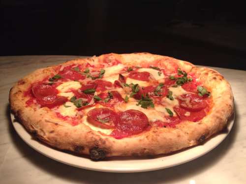 A freshly baked pizza topped with pepperoni, mozzarella, and fresh basil on a white plate.