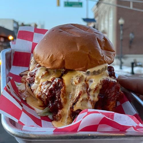 A close-up of a delicious burger with crispy chicken, drizzled sauce, and lettuce, served in a red and white checkered basket.