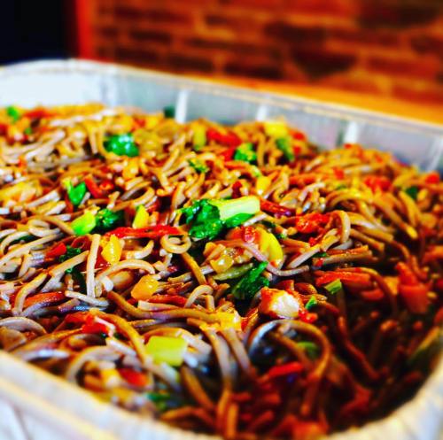 A close-up of a tray filled with colorful stir-fried soba noodles mixed with vegetables.