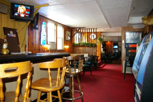 Interior of a bar with wooden decor, a TV showing news, and a view of the dining area in the background.