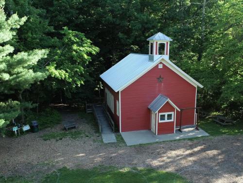 A small red building with a white roof and bell tower, surrounded by trees and gravel pathways.
