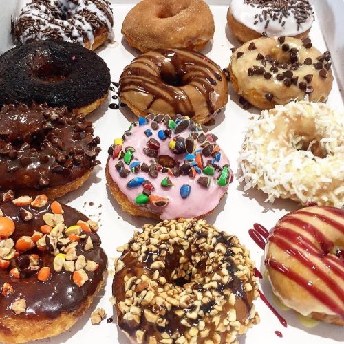 A variety of colorful donuts with different toppings, arranged in a box, including chocolate, sprinkles, and coconut.