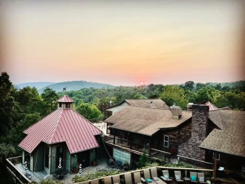 A scenic view of a rustic lodge at sunset, surrounded by lush green hills and a colorful sky.