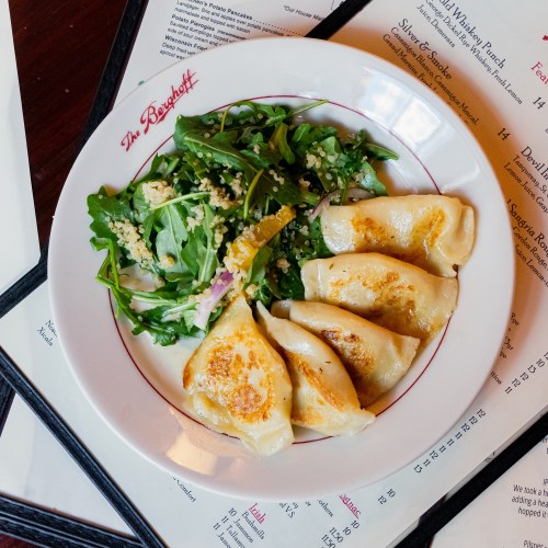 A plate of golden-brown dumplings served with a fresh arugula salad and quinoa, on a restaurant table.