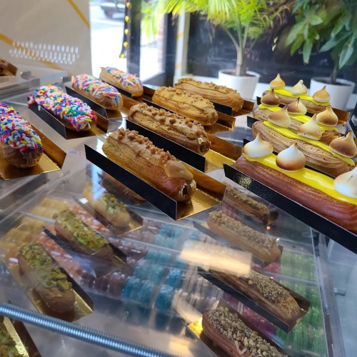 A display of colorful eclairs and pastries, featuring various toppings like sprinkles, nuts, and meringue.