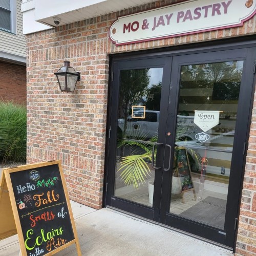 Entrance of Mo & Jay Pastry with a welcoming sign about fall scents and a potted plant beside the door.