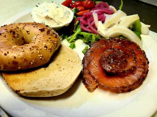 A plate with a sesame bagel, smoked salmon, cream cheese, and a side of mixed vegetables and pickled onions.