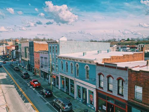 A vibrant street scene with colorful buildings, parked cars, and a blue sky filled with clouds.