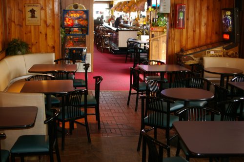 A cozy restaurant interior with empty tables, wooden walls, and arcade games in the background.