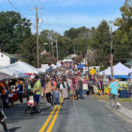 A bustling street fair with numerous tents and a large crowd enjoying the event under a clear blue sky.