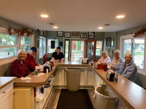 A cozy diner interior with six patrons seated at the counter, enjoying their meals and chatting.