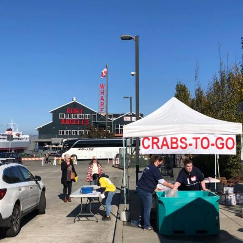 A seafood stand labeled "CRABS-TO-GO" at Port Angeles, with people buying crabs on a sunny day.