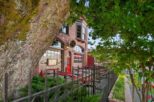 A brick building with large windows and a red door, framed by a tree and a decorative fence.