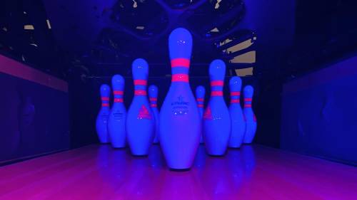 Glowing bowling pins in a dark alley, illuminated with blue and pink lights.
